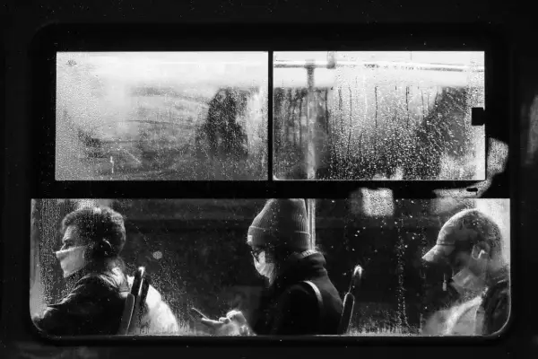 Trzej pasażerowie w maseczkach w deszczowy dzień, uchwyceni przez współczesnych polskich fotografów.